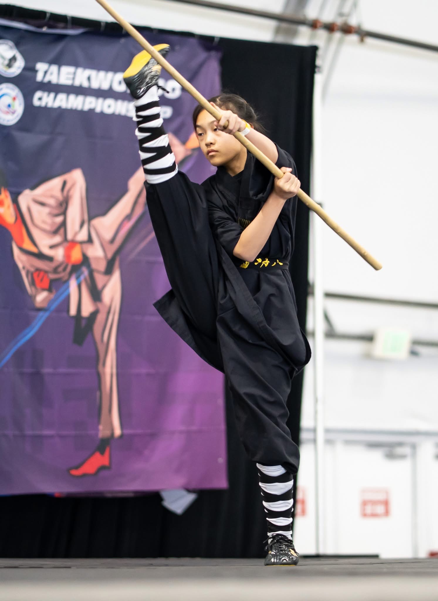 Student performing high kick with staff
